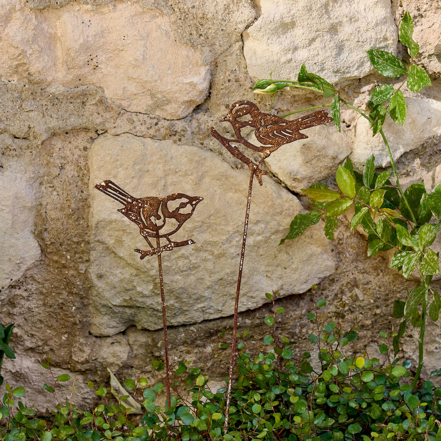 Gartenstab 2er Set Pelvaron Dekorative rostige Metallvögel auf Stäben für den Garten vor einer Steinmauer