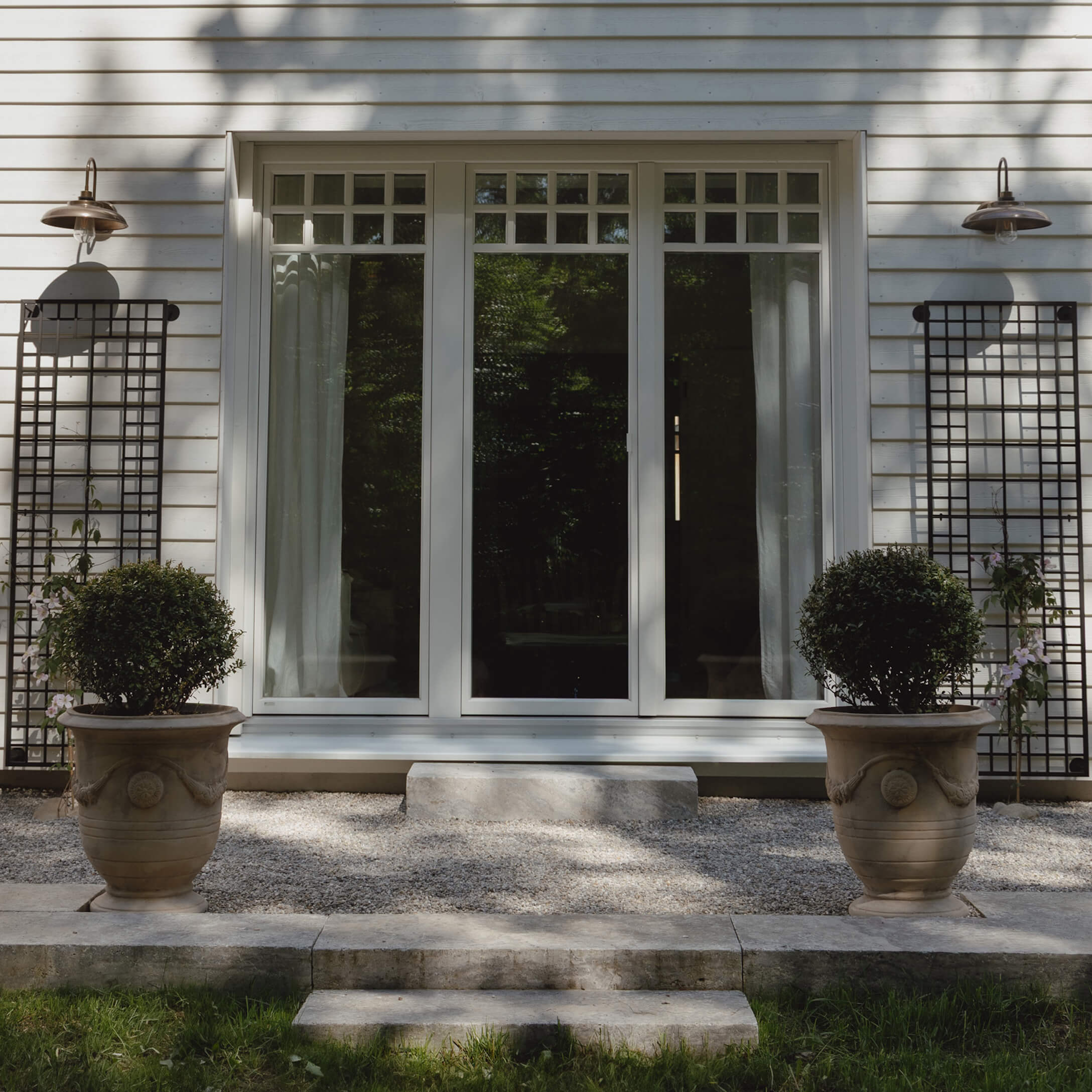 Eingang mit weißen Türen und zwei großen Steintöpfen mit grünen Pflanzen auf Kiesboden