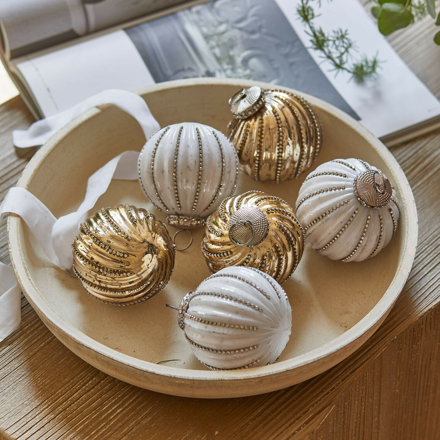 Weihnachtskugel 6er Set Shaela Set aus weißen und goldfarbenen Weihnachtskugeln mit metallischem Glanz in einer runden Schale auf Holztisch