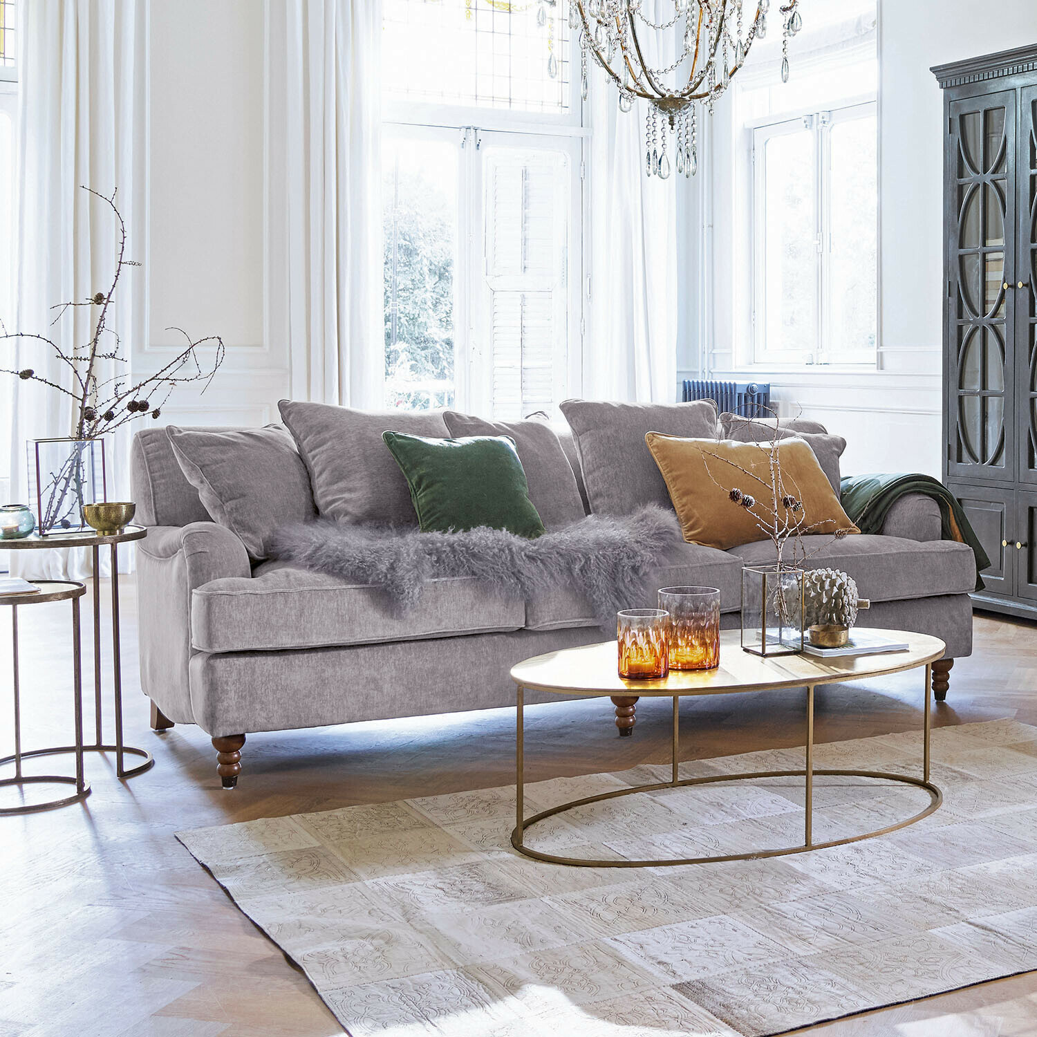 Sofa Isa Graues Sofa aus weichem Stoff mit bunten Kissen und ovalem Couchtisch im hellen Wohnzimmer