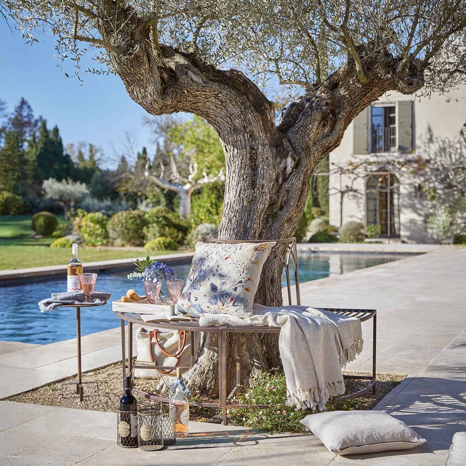 Metallbank um Baum mit Kissen und Decke am Pool im Garten mit Weinflaschen