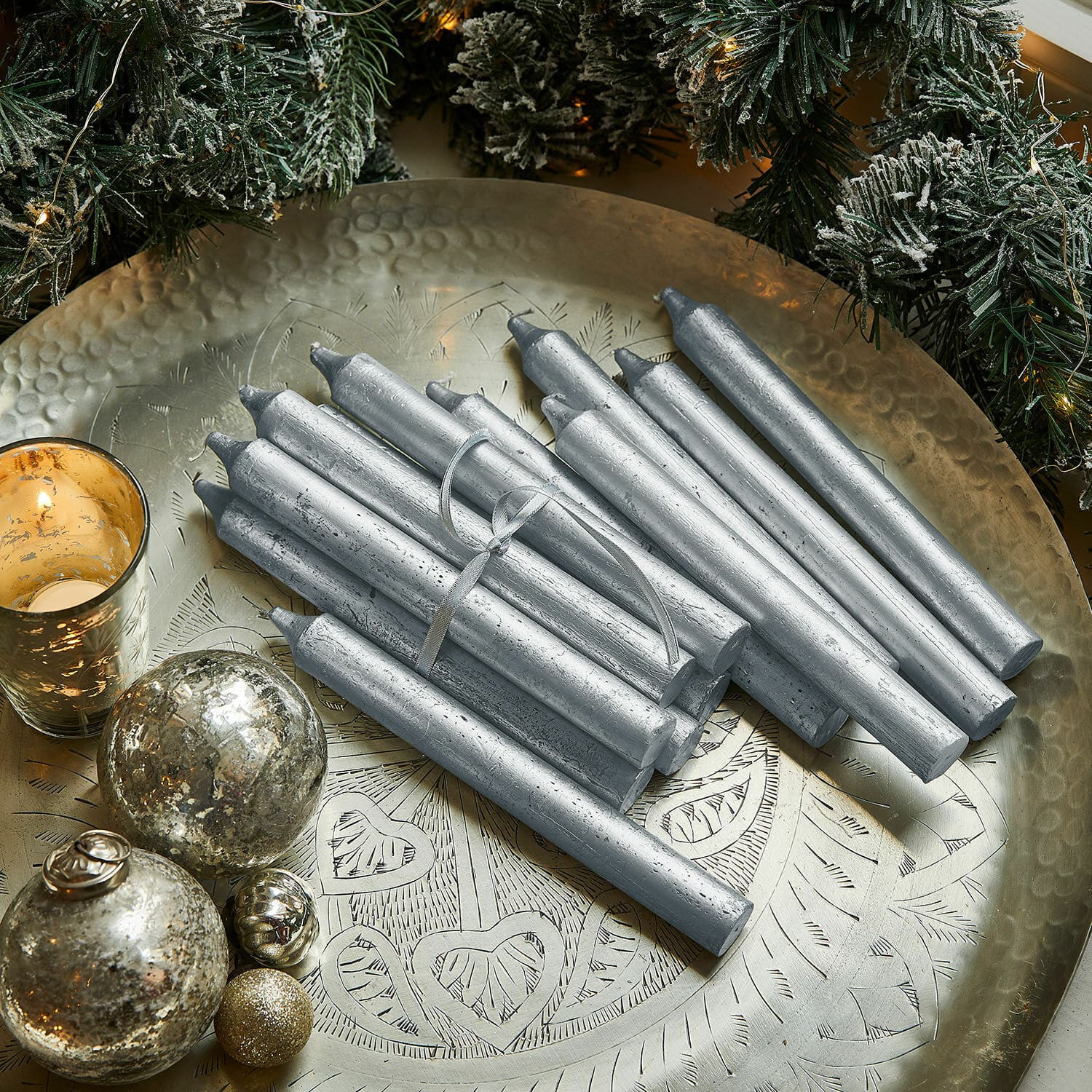 Kerze 20er Set Lysarion Silberne Stabkerzen auf einer Messingplatte mit Weihnachtsdeko und Kugeln vor grünen Zweigen
