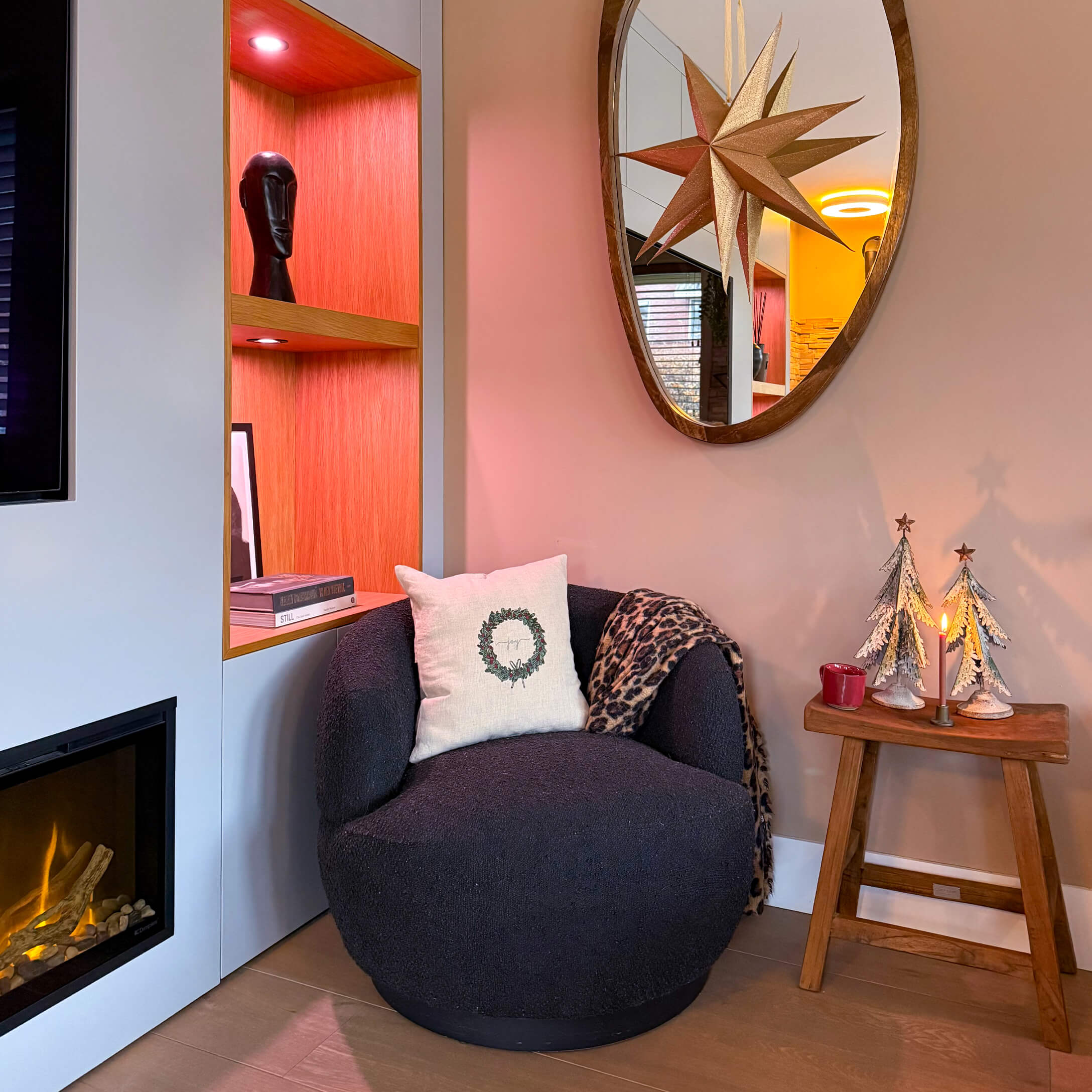 Schwarzer weicher Sessel mit Kissen und Decke neben Kamin und Holzhocker mit Weihnachtsdekoration