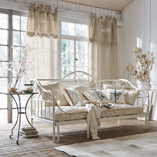 Weiße Metallsofa mit beigen Kissen und hellen Vorhängen in rustikalem Wohnzimmer