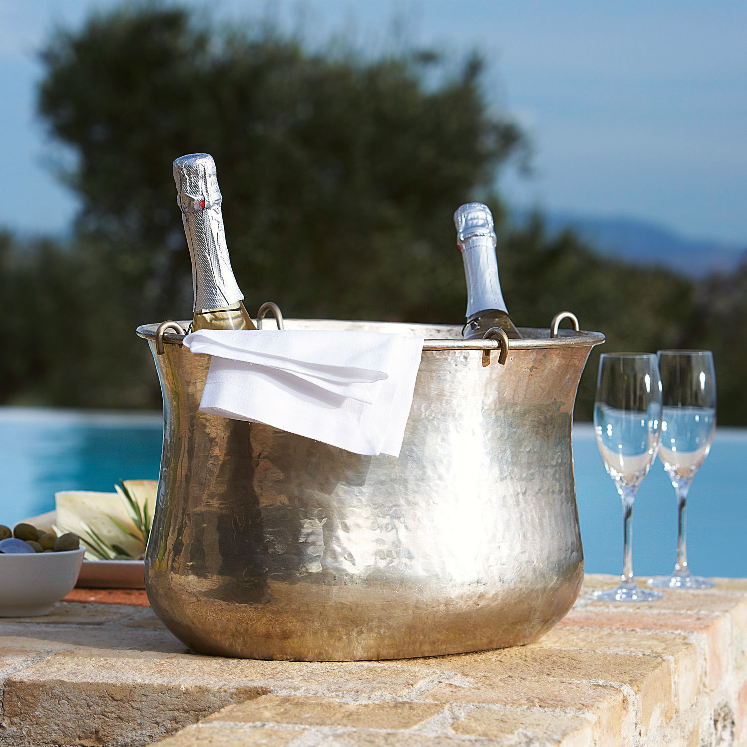 Sektkühler Montgomery Messer gehämmerter Kupfer-Eiseimer mit zwei Champagnerflaschen und weißer Serviette auf Terrasse