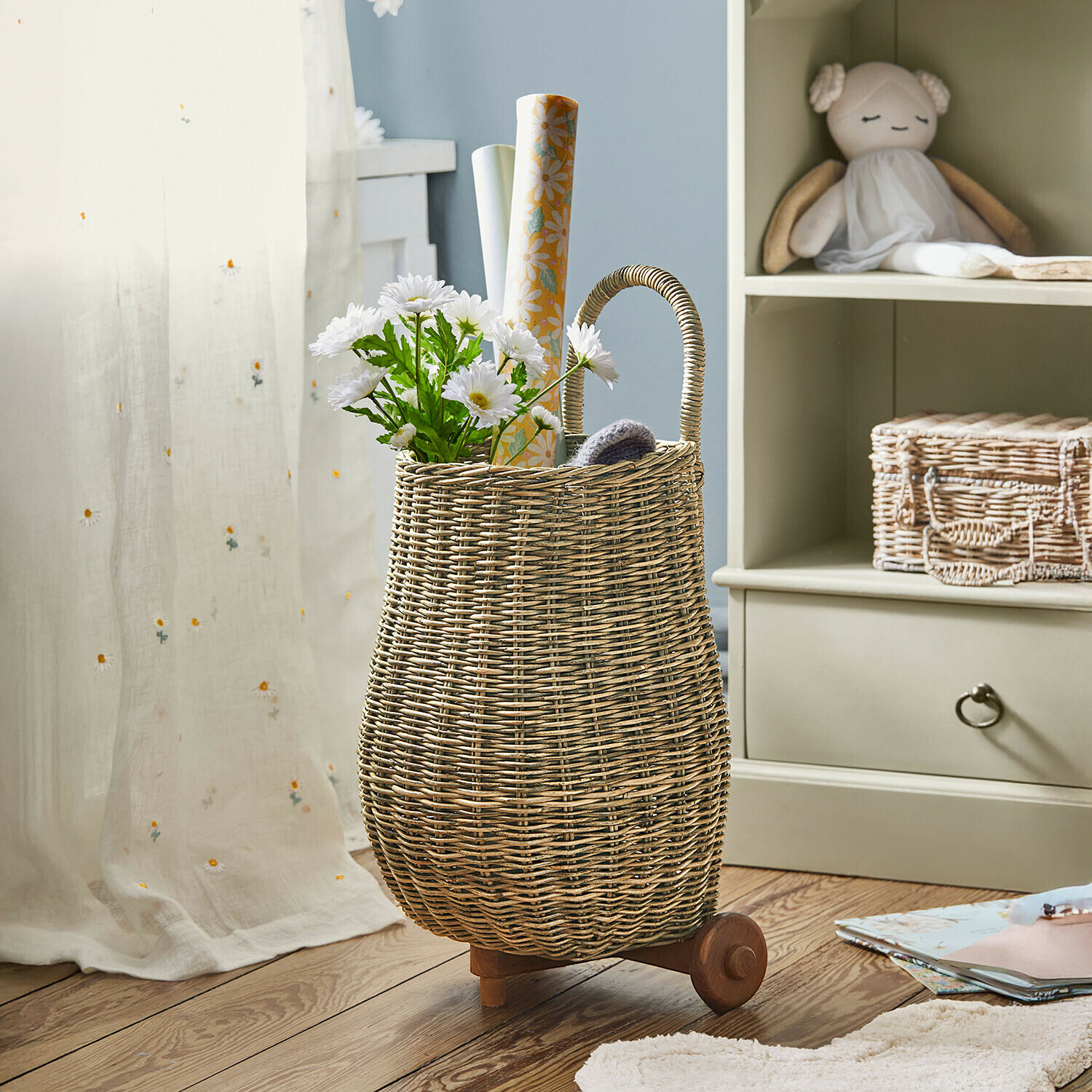 Natürlicher Korb aus Weide auf Rollen mit Griff, gefüllt mit weißen Blumen und Dekorpapier