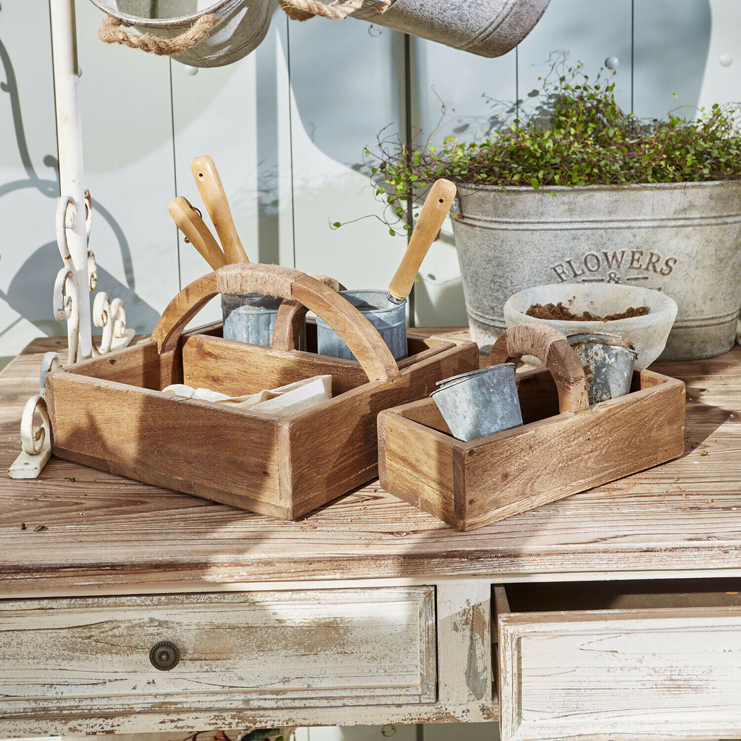 Holzkisten mit Griffen und Metalltöpfen auf Gartentisch für Gartenwerkzeuge und Pflanzzubehör