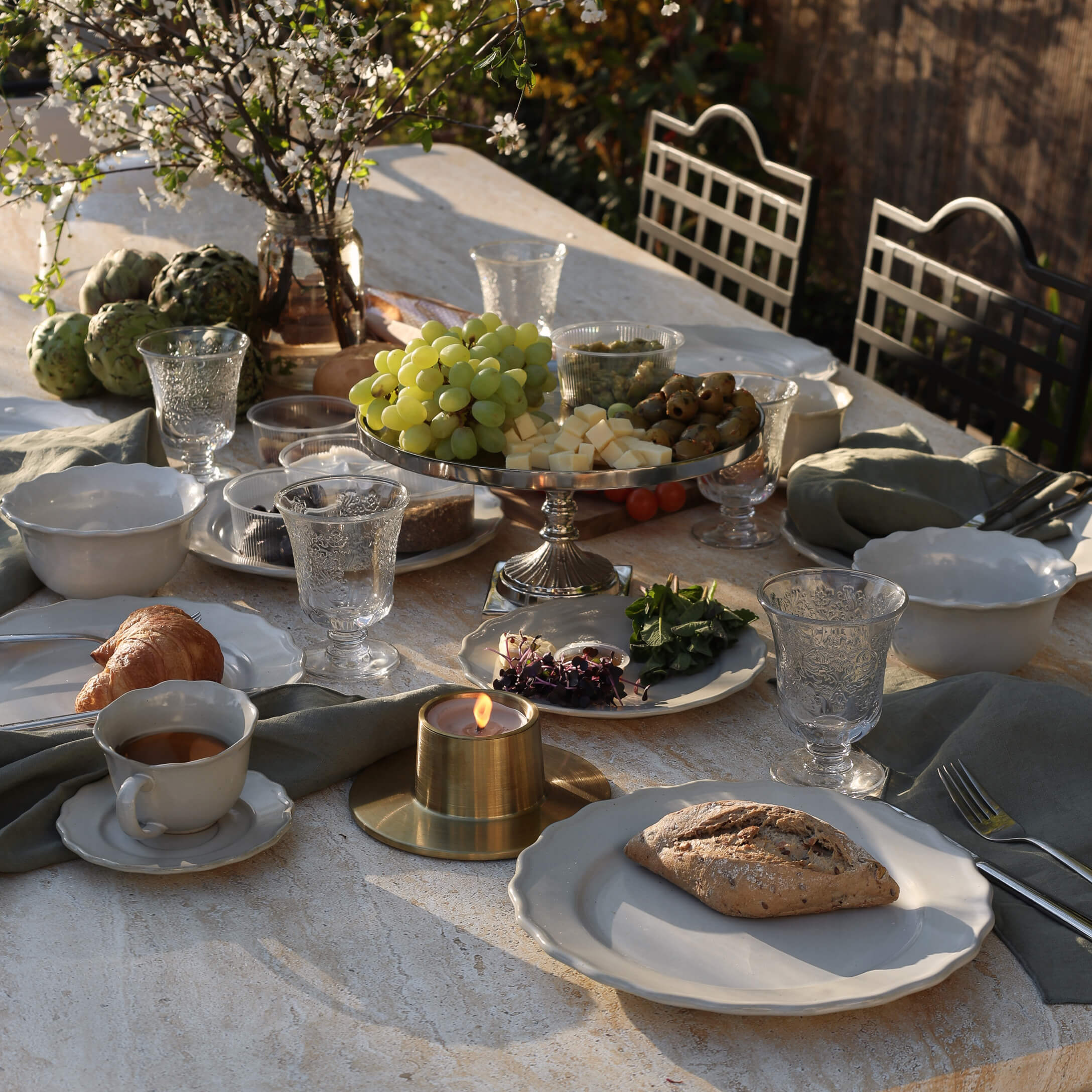 Steintisch mit weißem Geschirr, Kerze und Tablett mit Trauben, Käse und Oliven im Freien