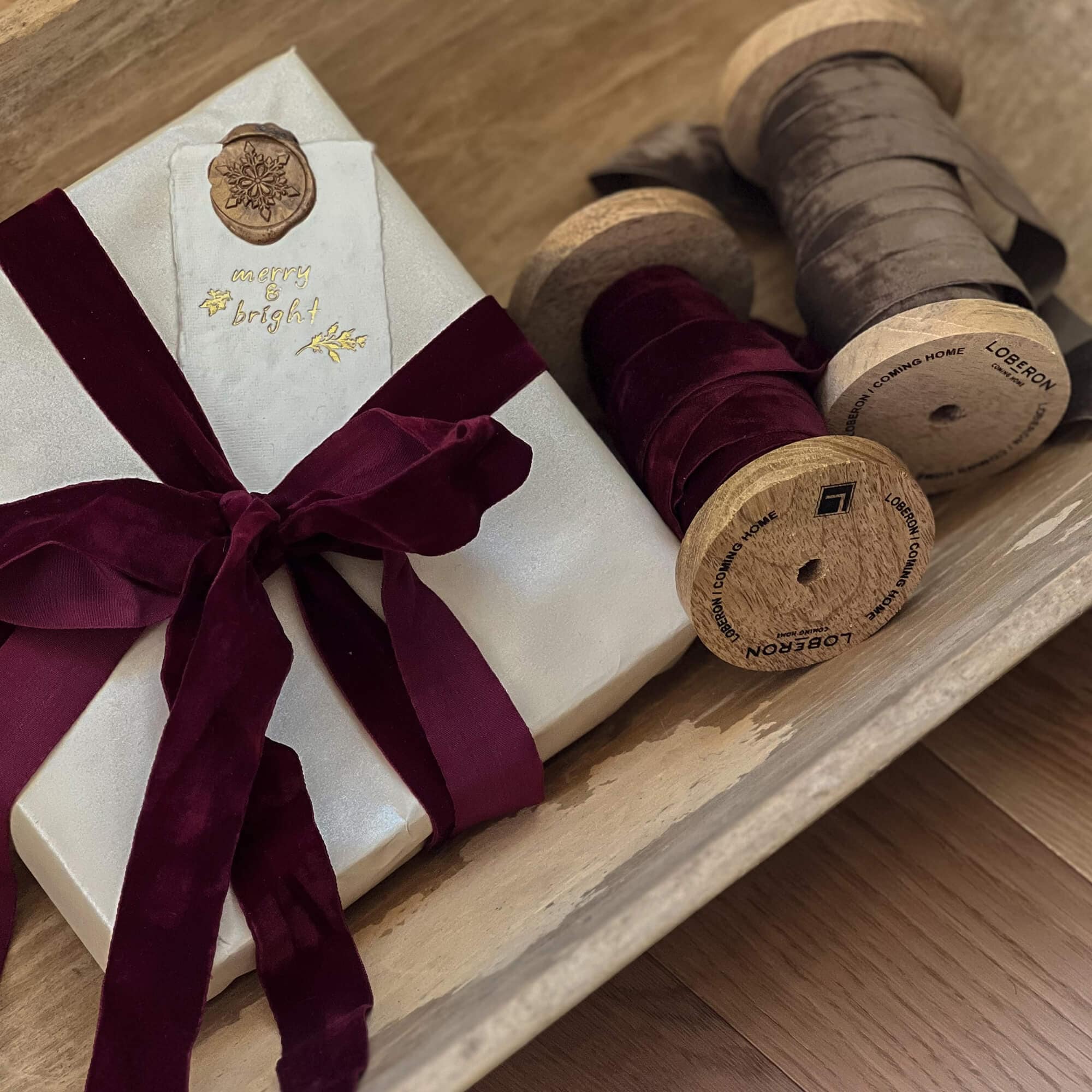 Geschenk in weißem Papier mit bordeauxrotem Samtband und Holzspulen mit Bändern dekoriert