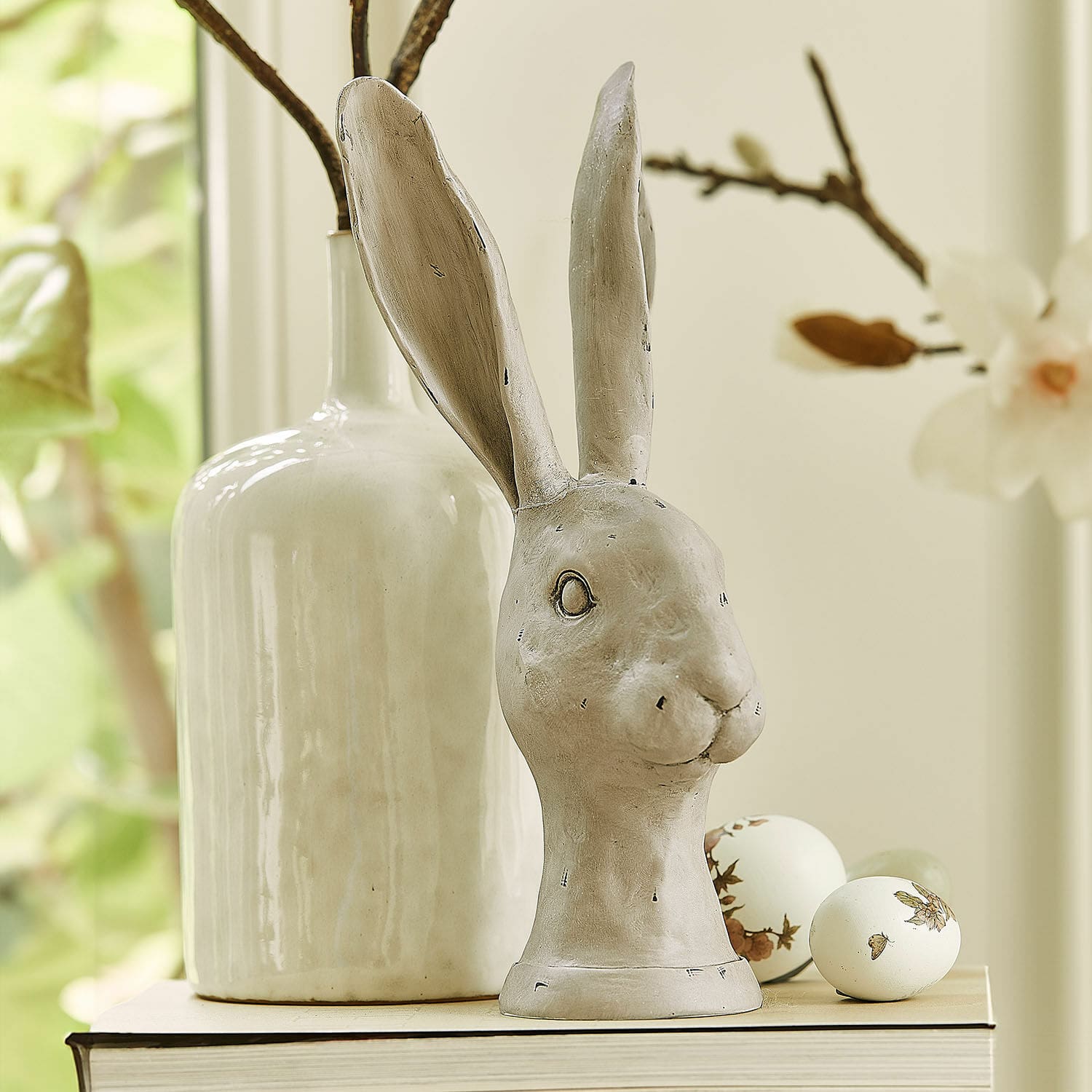 Hase Najirah Dekorative Hasenfigur aus grauer Keramik auf Buch mit verzierten Ostereiern