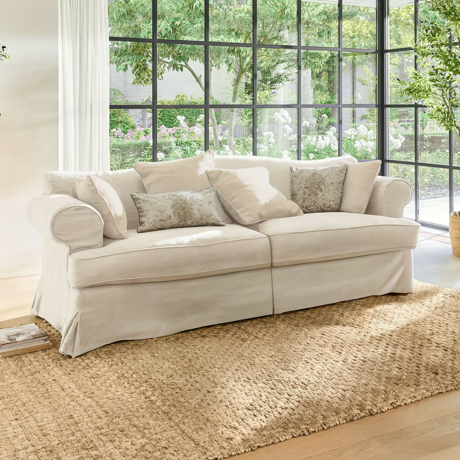 Sofa Dawnhurst Beiges Sofa aus Stoff mit dekorativen Kissen auf Naturteppich in hellem Wohnzimmer mit großen Fenstern