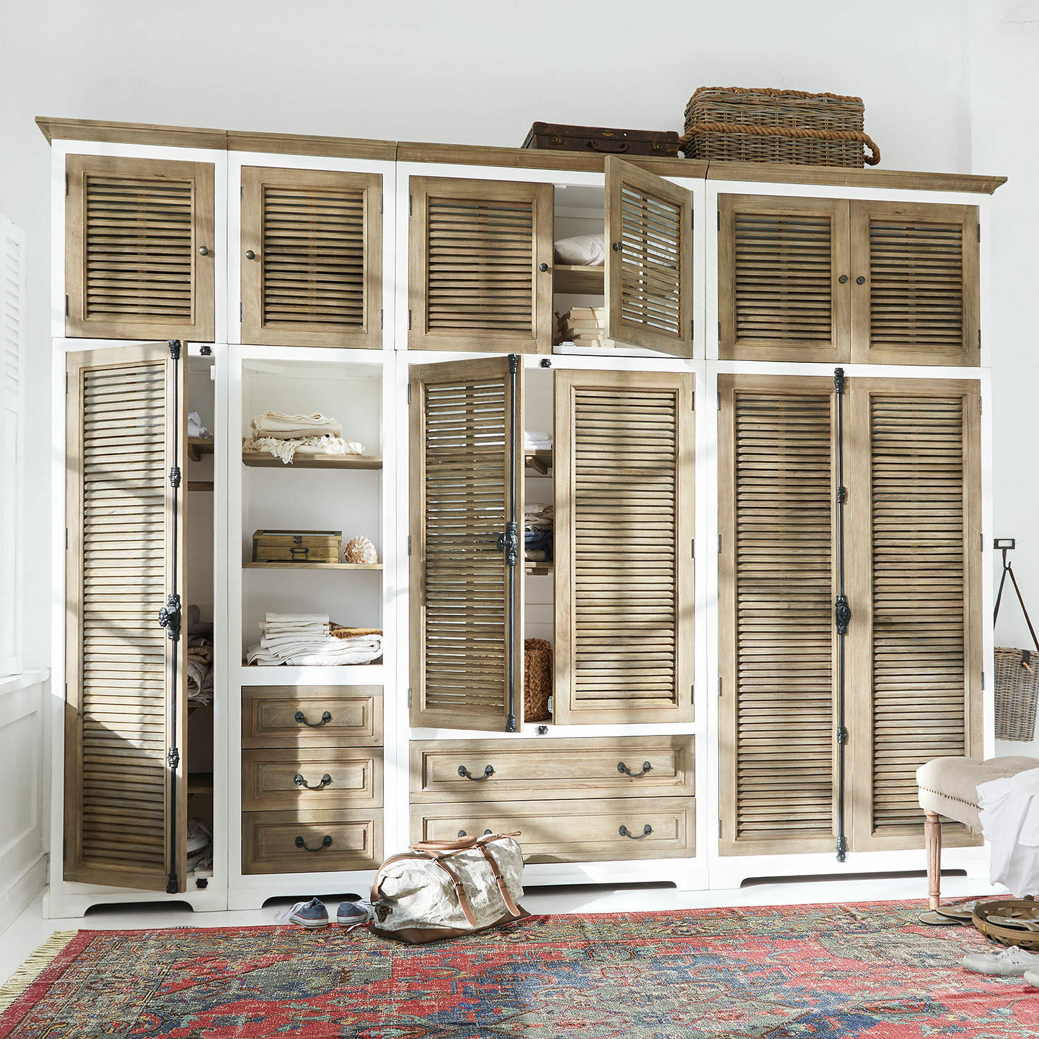 Schrank-Set Daviau Großer Holzschrank in Weiß und Natur mit Lamellentüren und Schubladen auf buntem Teppich.