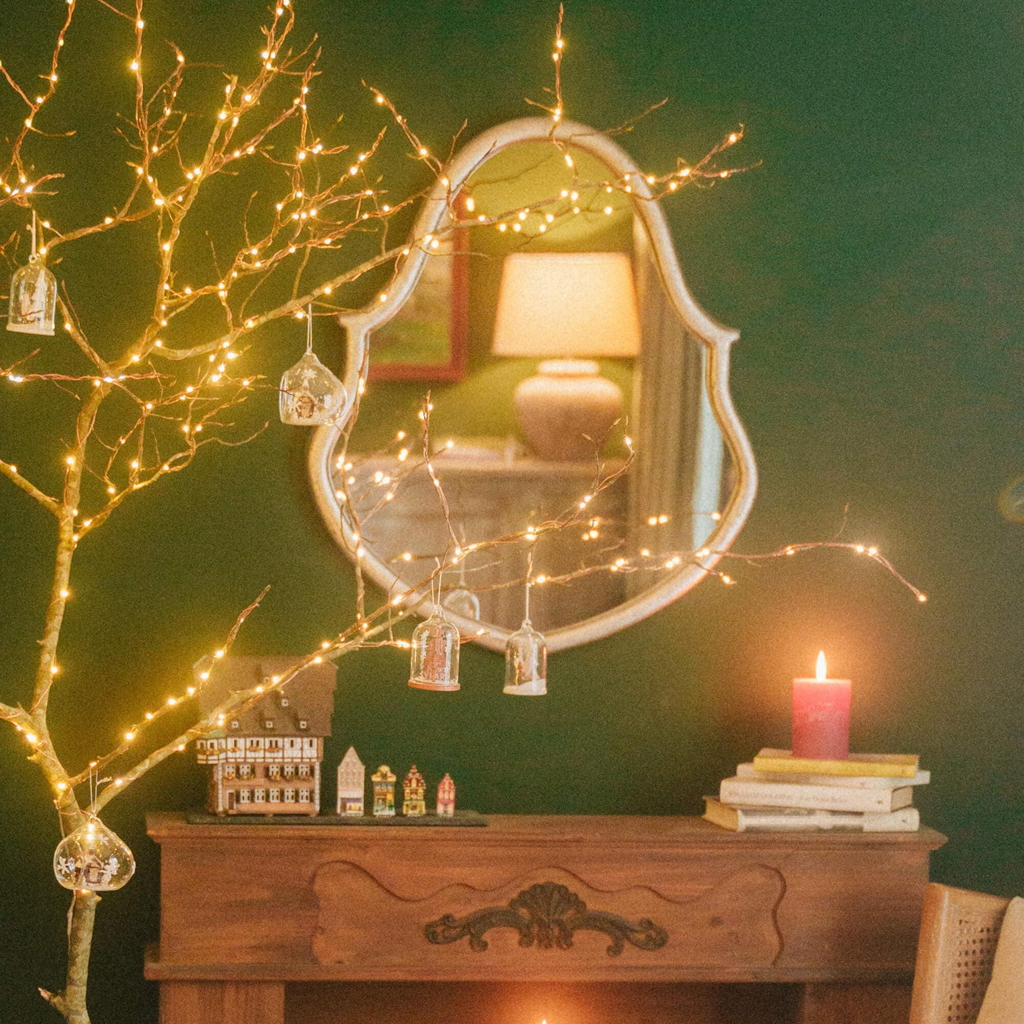 Weihnachtliche Dekoration mit LED-Lichterzweigen vor grünem Wandspiegel im Wohnzimmer