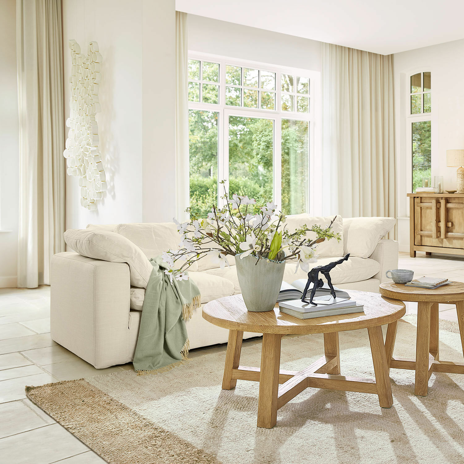 Sofa Queensbridge Helles Stoffsofa mit grünem Plaid und runder Holzcouchtisch in einem hellen Wohnzimmer