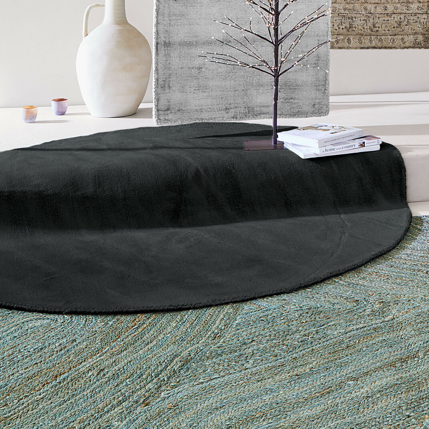 Runder schwarzer Teppich aus weichem Material in hellem Raum mit Dekorationen und Büchern
