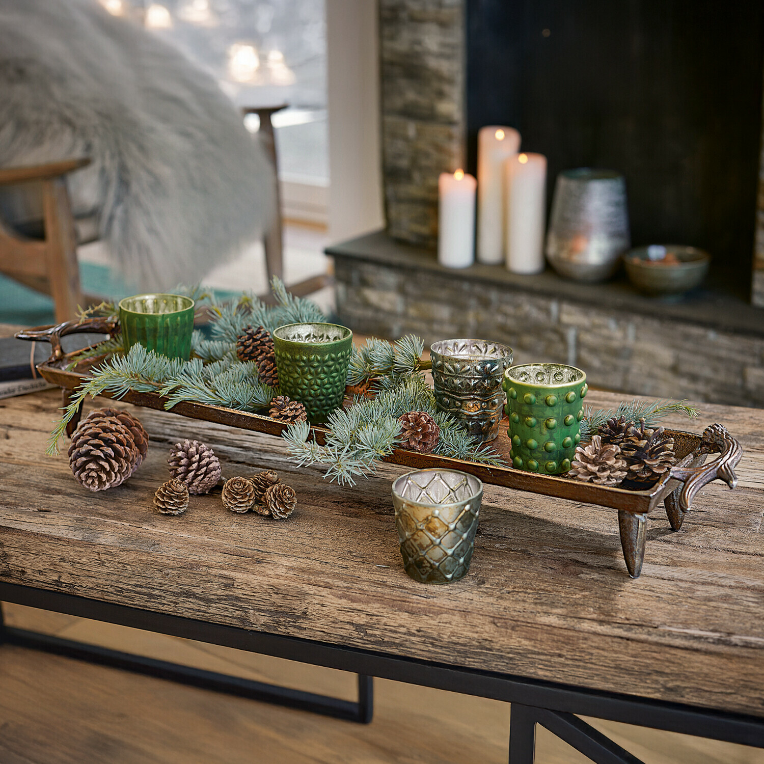 Dekoratives Metalltablett mit grünen und silbernen Glas-Teelichthaltern und Kiefernzapfen auf Holztisch