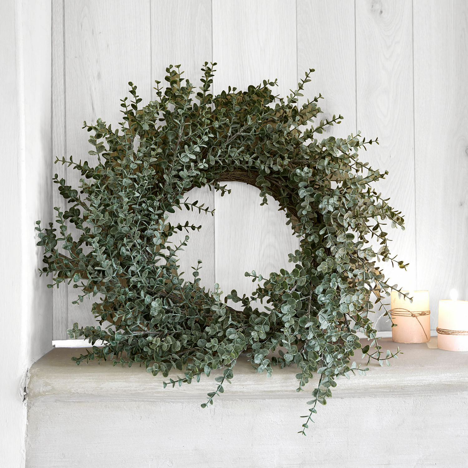 Dekorativer Kranz aus grünen Eukalyptusblättern auf hellem Regal mit zwei Kerzen