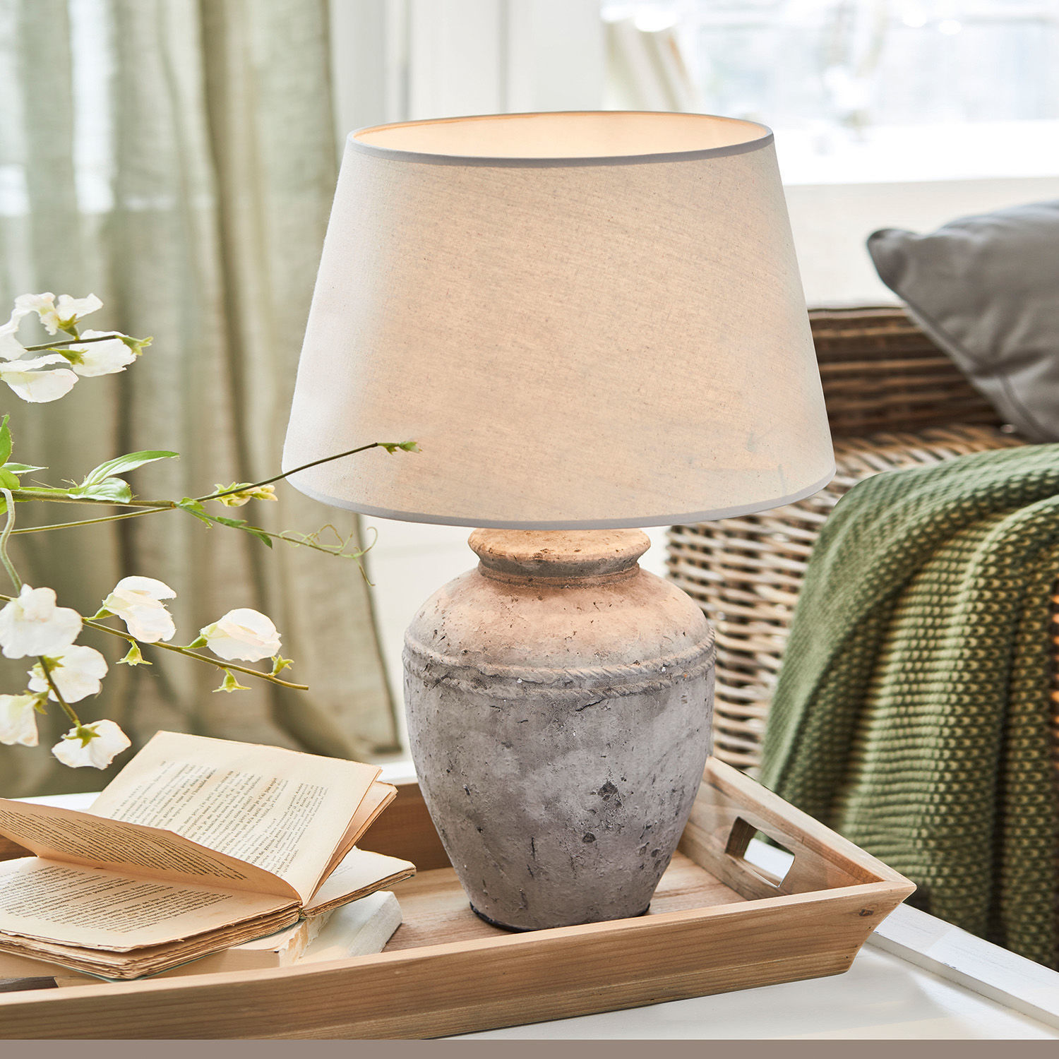 Tischlampe aus grauer Keramik mit beigem Lampenschirm auf Holztablett im Wohnzimmer