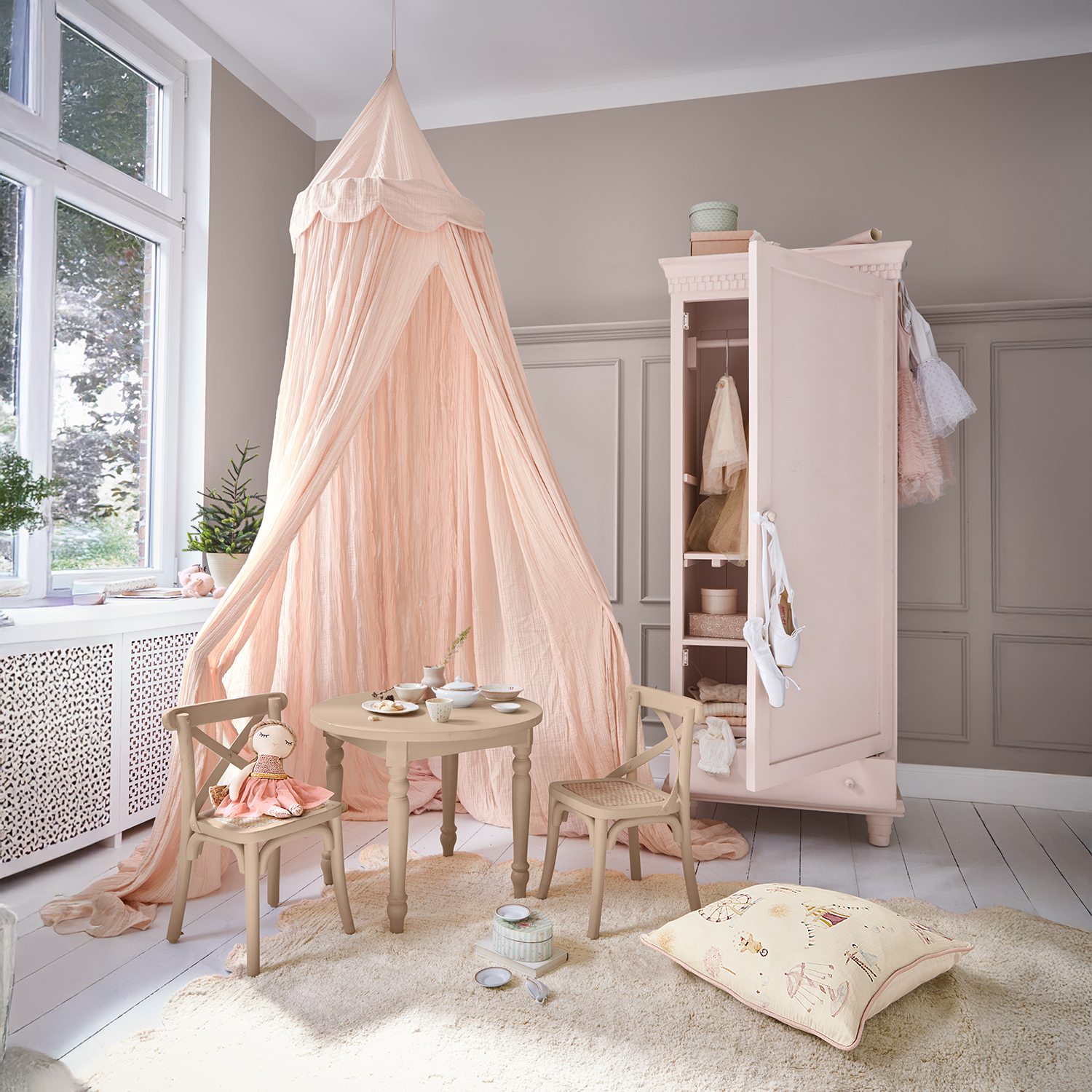 Gemütliches Kinderzimmer mit rosa Baldachin, runden Holztisch, Stühlen und offener rosa Garderobe