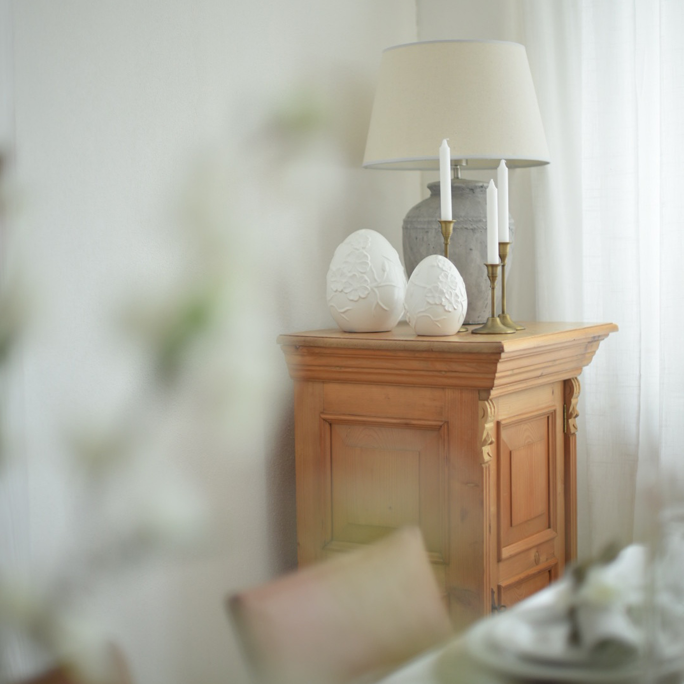 Holzschrank mit Lampe, Kerzen und weißen Keramik-Eierdekorationen in hellem Raum