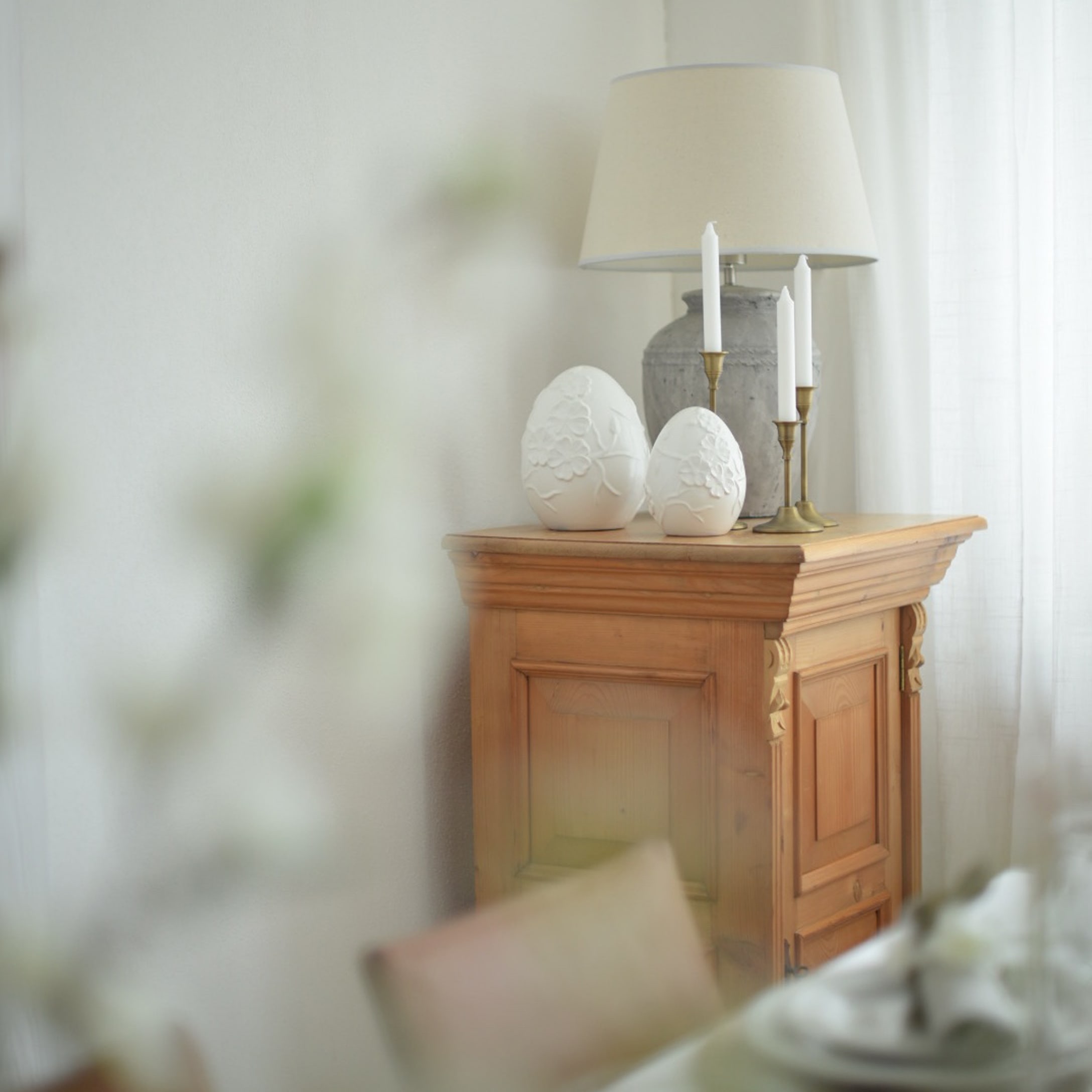Holzschrank mit Lampe, Kerzen und weißen Keramik-Eierdekorationen in hellem Raum