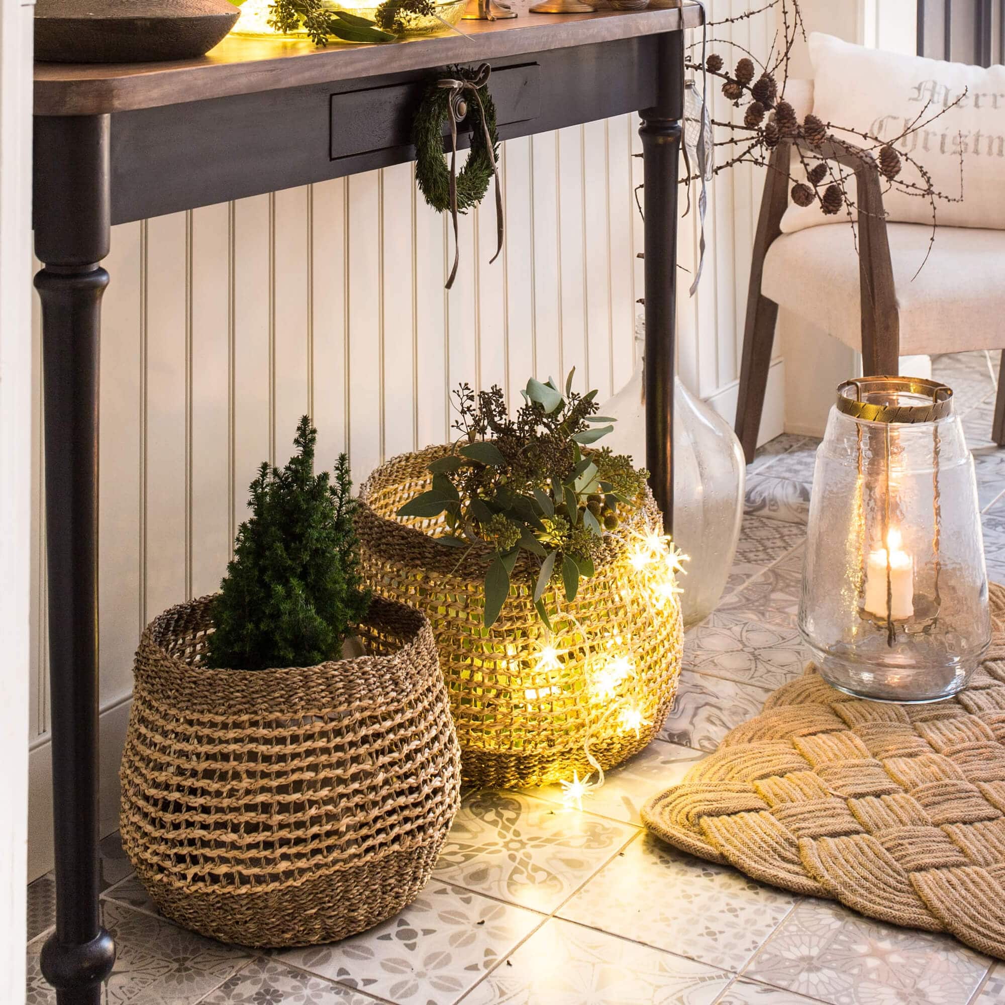 Dekorative Körbe aus Naturmaterial mit grünen Pflanzen und LED-Lichterkette auf dem Boden
