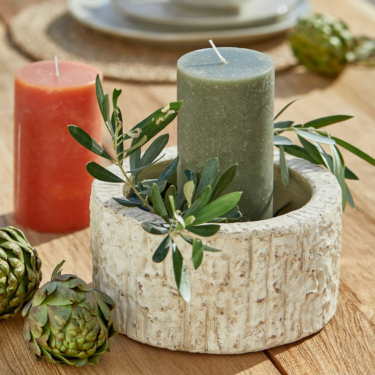Schale Continas Runder Kerzenhalter aus beigem Stein mit grüner Kerze und Blattdeko auf Holztisch