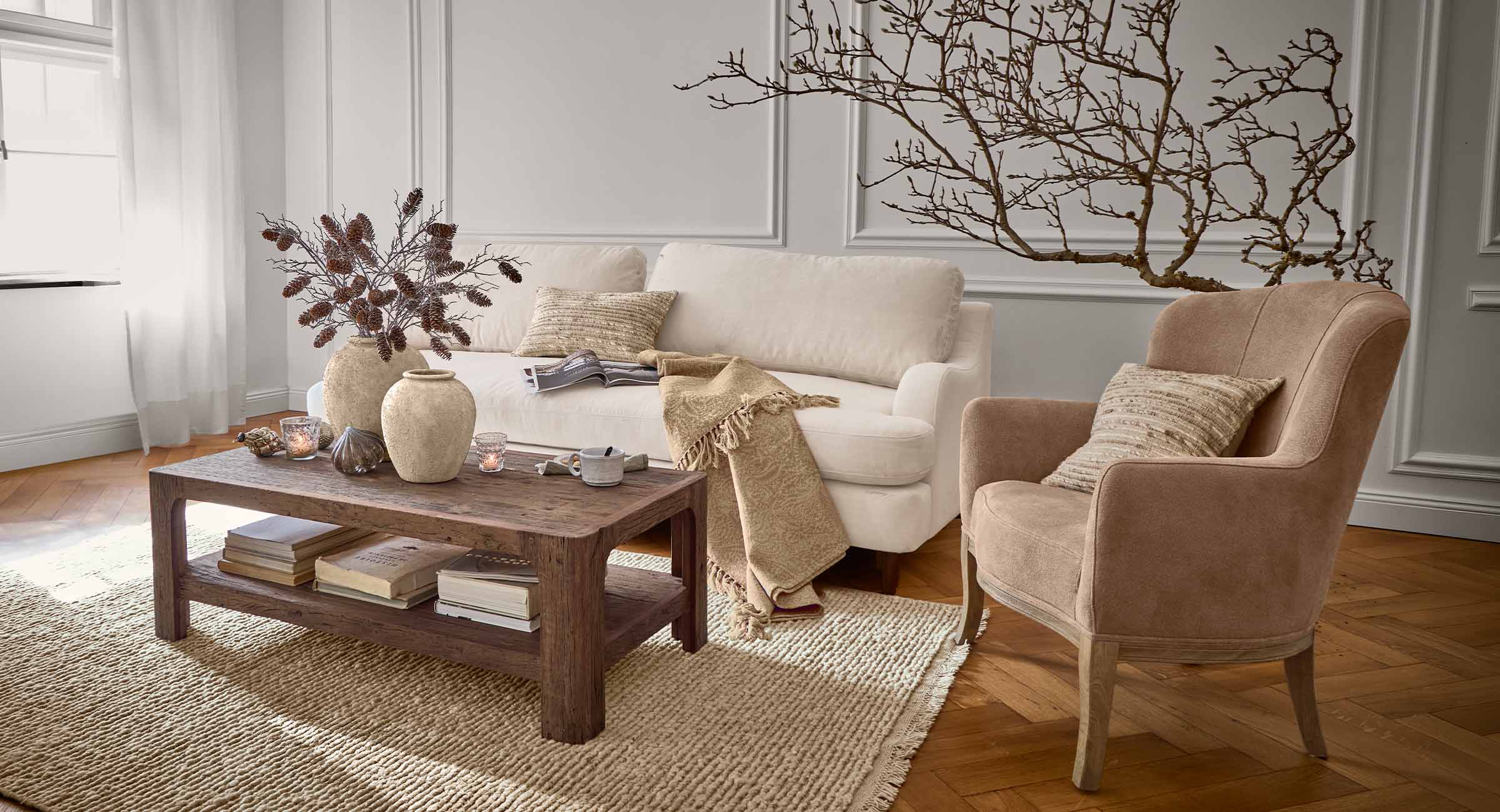 Gemütliches Wohnzimmer mit beigem Sofa, braunem Sessel und Holzcouchtisch auf Naturfaserteppich