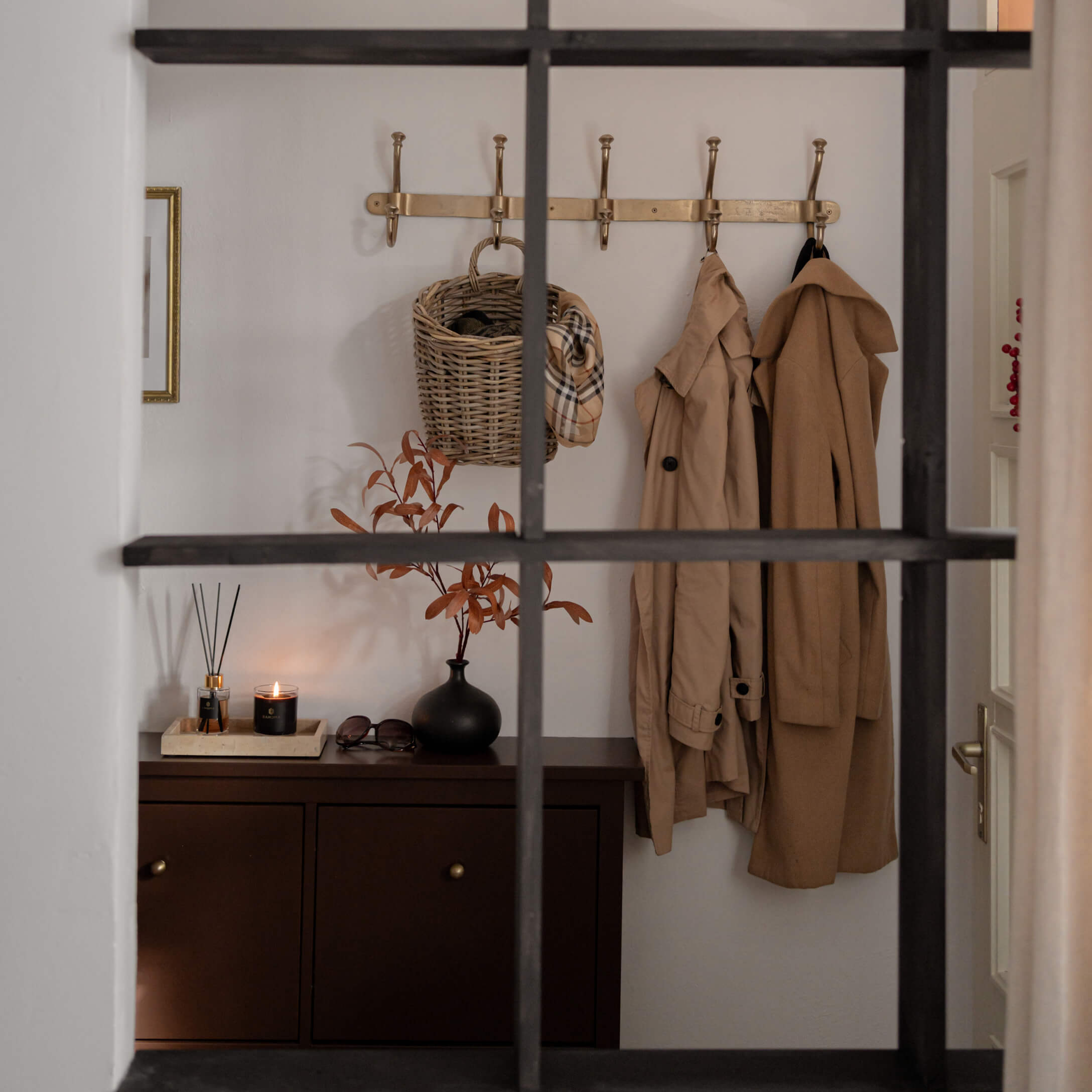 Flur mit braunem Schrank, beigen Mänteln und Korb an goldener Garderobe