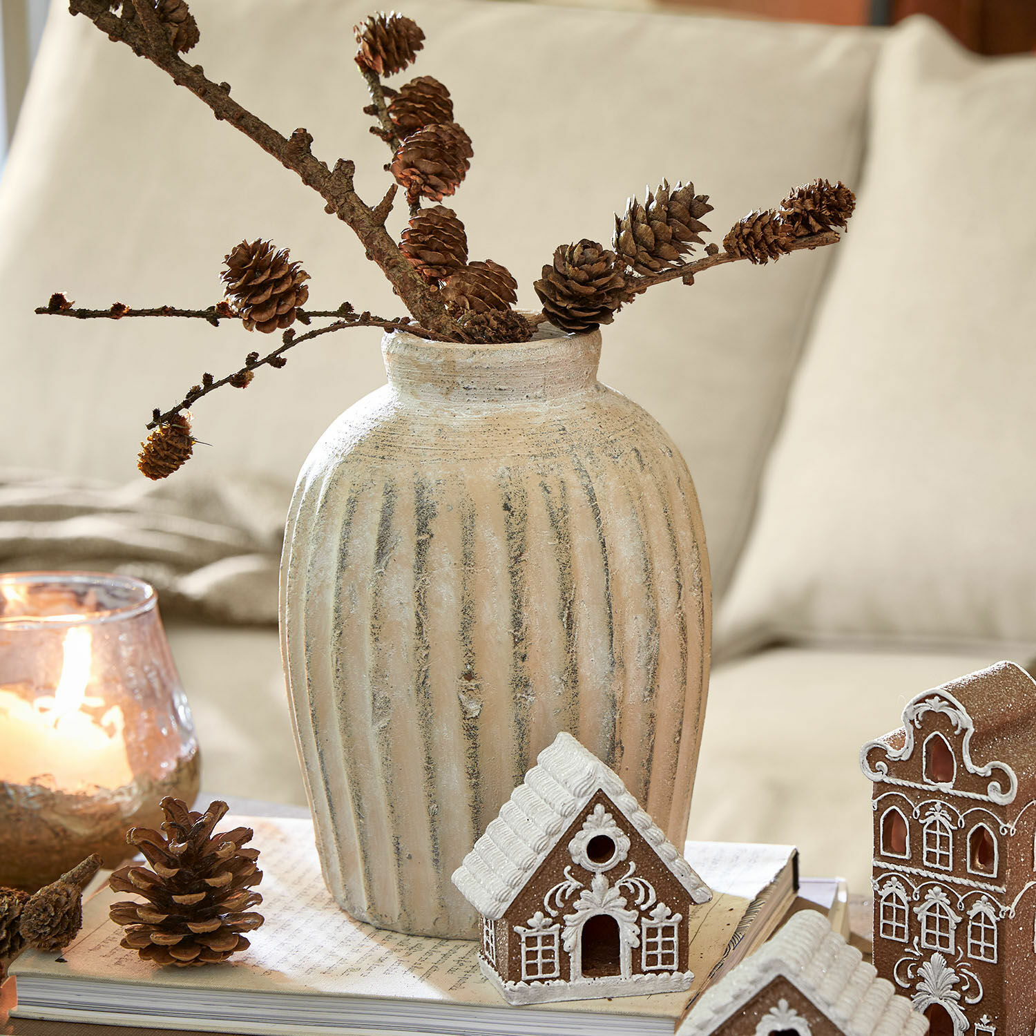 Beiger Keramikvase mit vertikalen Rillen, Zweige mit Zapfen, weihnachtliche Dekoration mit Lebkuchenhäusern