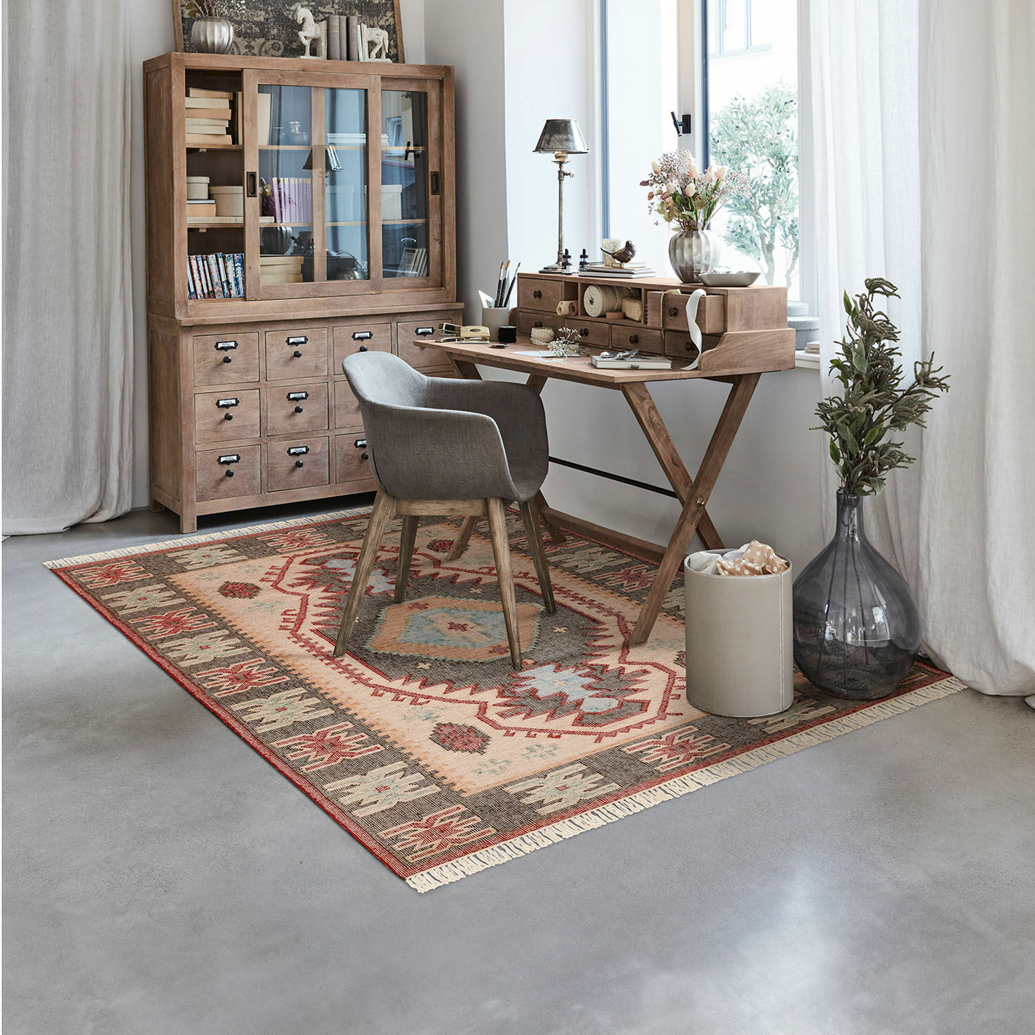 Teppich Frída Gemütliches Arbeitszimmer mit Holzschreibtisch und grauem Polsterstuhl auf buntem Musterteppich