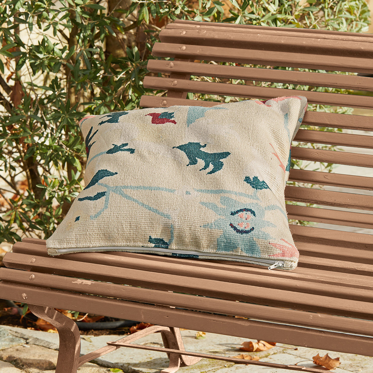 In- & Outdoor-Kissenhülle Sorbey Beige Dekokissen mit buntem Muster auf brauner Gartenbank aus Holz