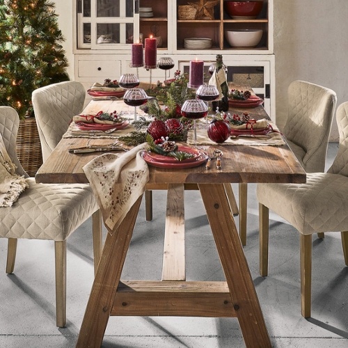 Holztisch mit beigen, gesteppte Stühlen und festlicher Weihnachtsdekoration mit roten Kerzen und Weingläsern