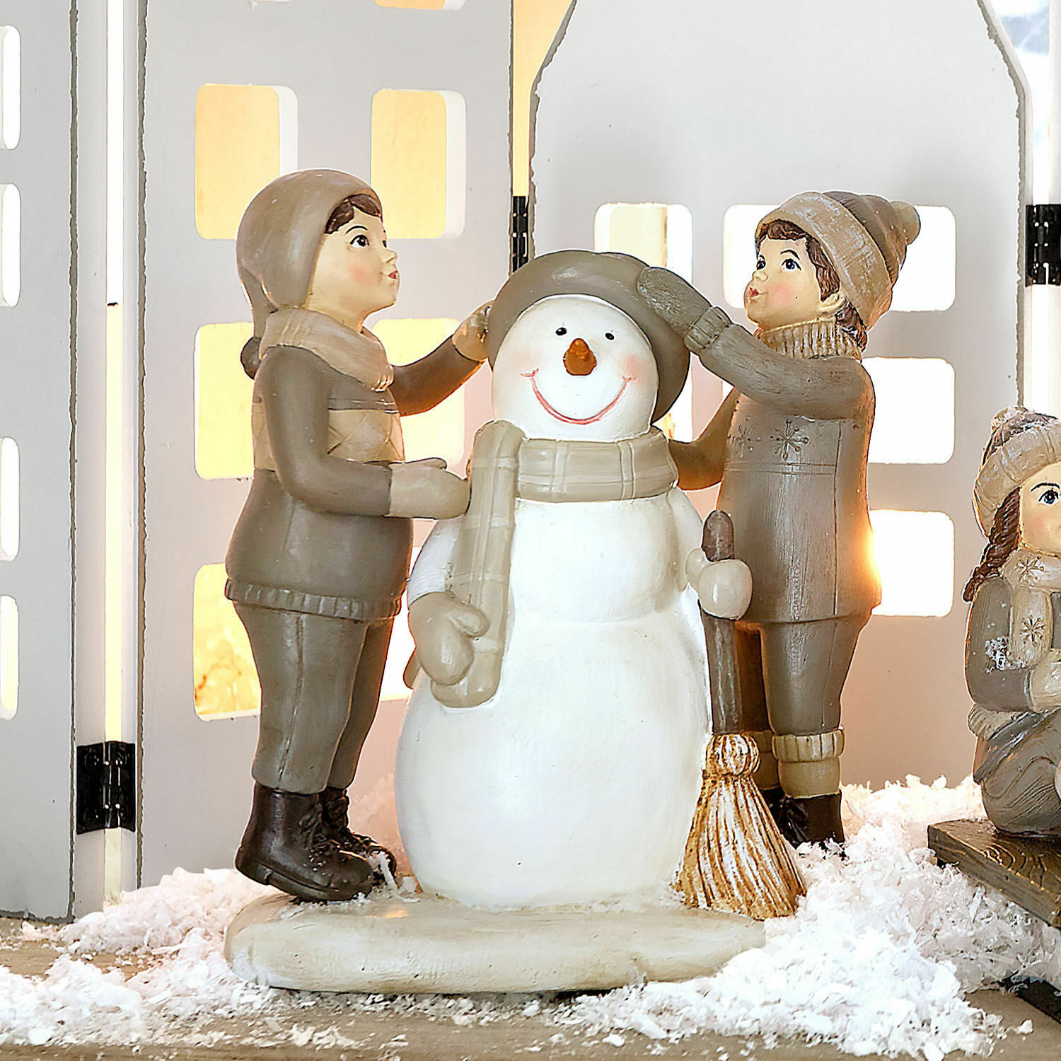 Deko-Figur Elvirette Figuren von Kindern, die einen Schneemann aus Material in Beige- und Brauntönen auf Dekoschnee anziehen