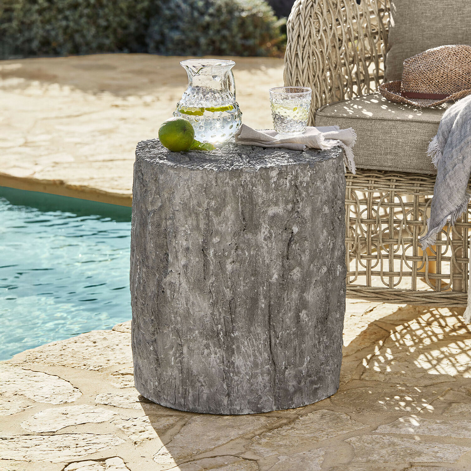 Grauer Beistelltisch aus Beton mit Holzstruktur neben Rattansessel am Pool