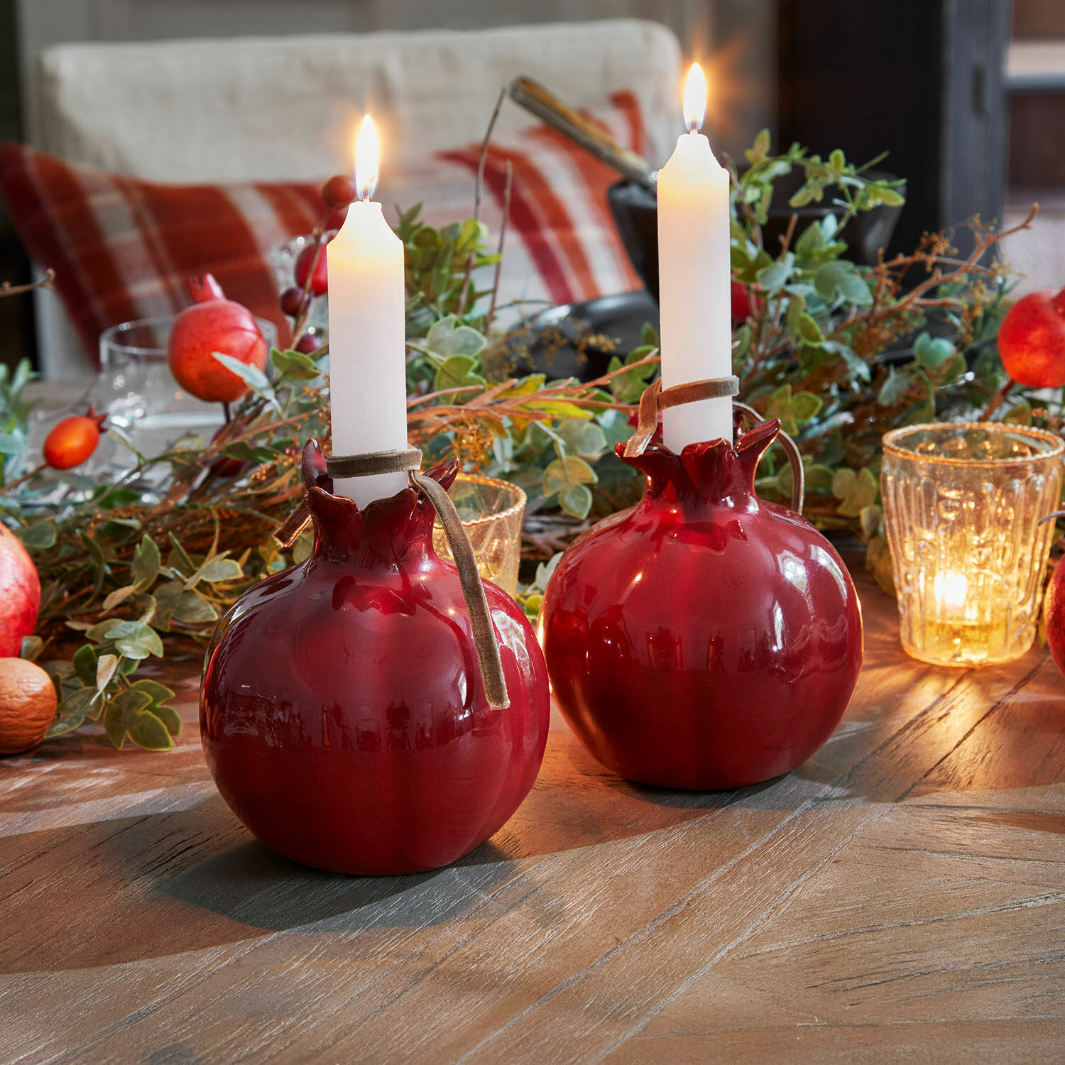 Zwei rote Keramik-Kerzenhalter in Granat-Form mit weißen Kerzen auf Holztisch mit Dekoration