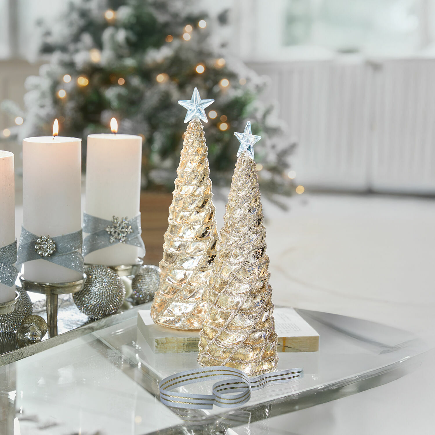 Deko-Baum 2er Set Glitter Zwei goldene Weihnachtsbaum-Dekorationen mit Sternen oben auf Glastisch mit weißen Kerzen und festlichem Hintergrund