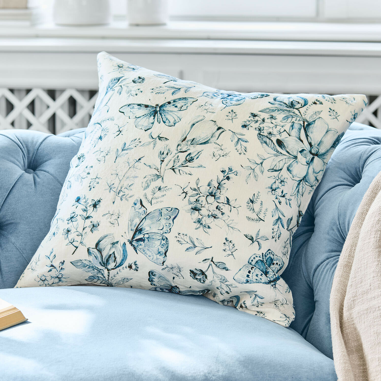 Dekoratives Baumwollkissen in Creme mit blauem Schmetterlings- und Blumenmuster auf hellem Hintergrund