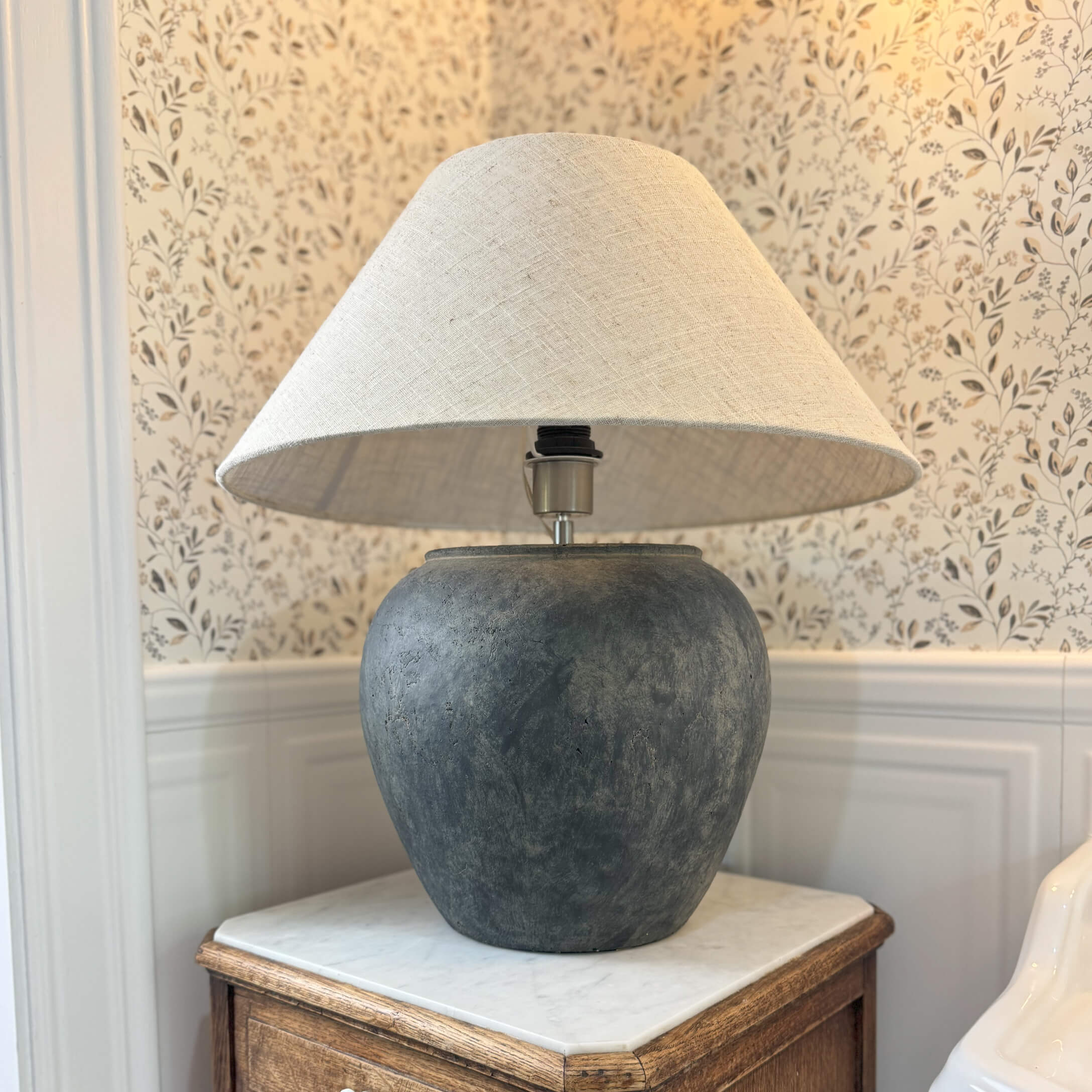 Tischlampe aus dunkelgrauer Keramik mit beigem Lampenschirm auf Holztisch in klassischem Raum