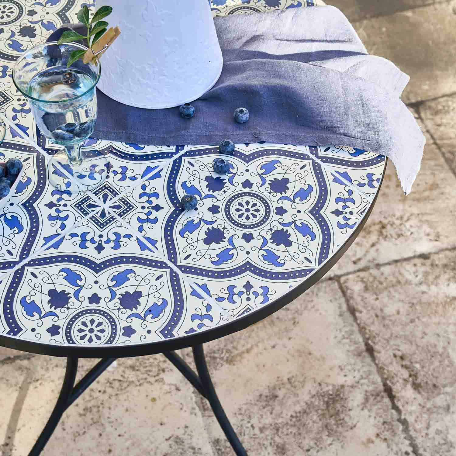Runder Tisch mit blau-weiß gemustertem Keramik-Tischplatte, grauem Tuch und verstreuten Heidelbeeren