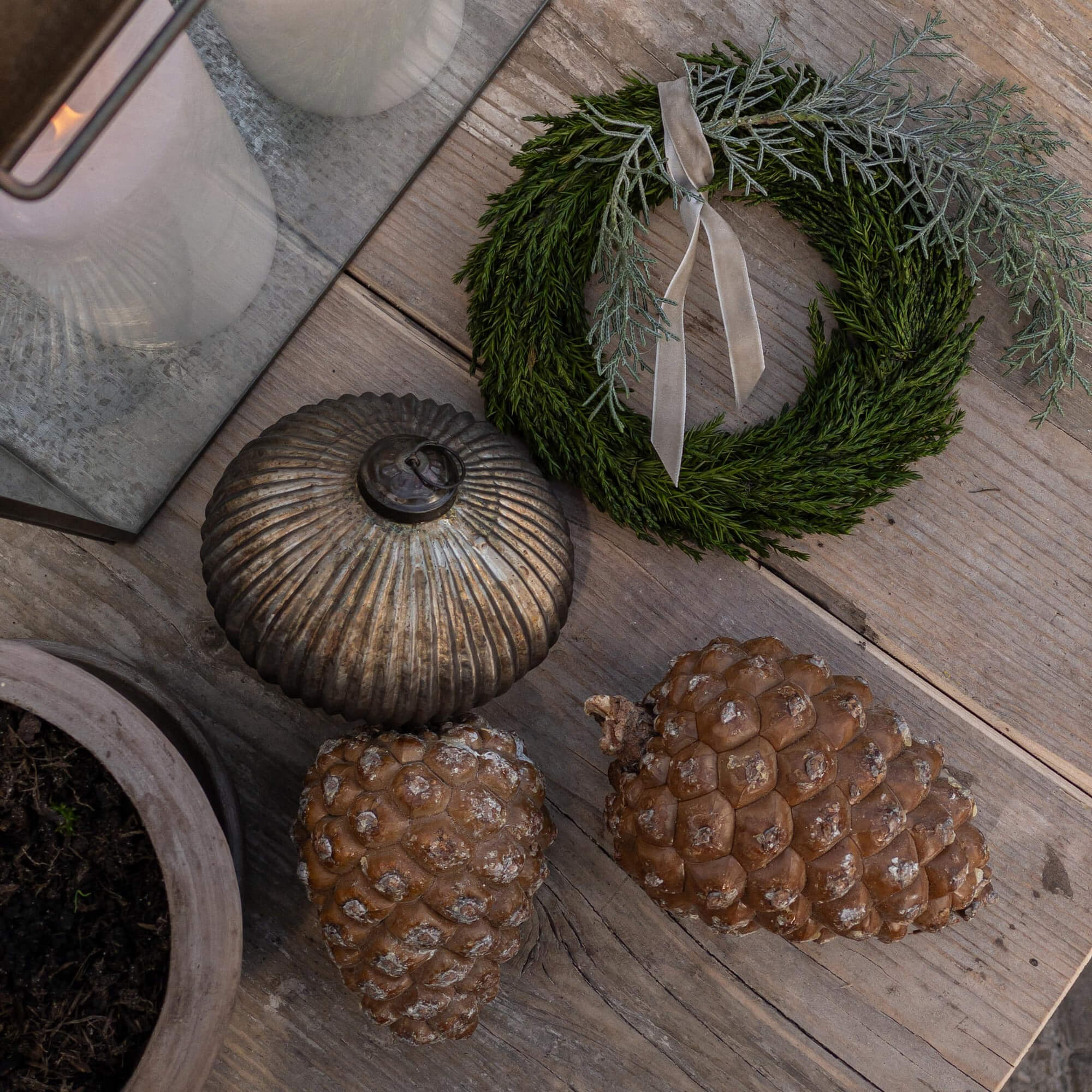 Dekorativer Kranz aus grünen Zweigen mit grauem Band und natürliche Kiefernzapfen auf Holztisch